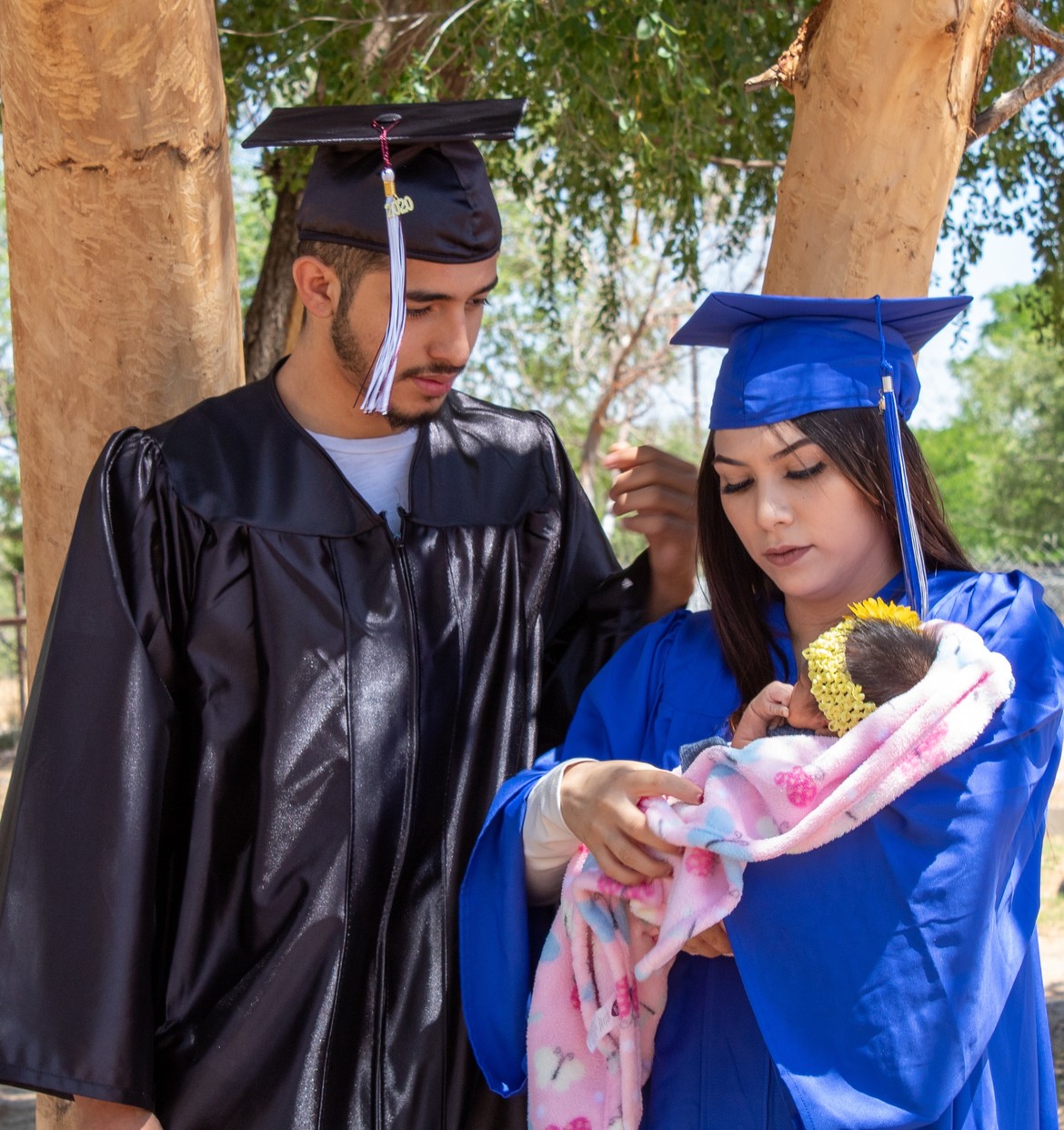 A young man and woman care for their new child in graduation clothes