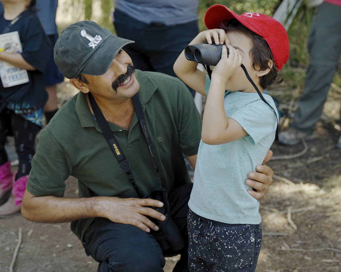 Father smiling as young child who is looking through binoculars.