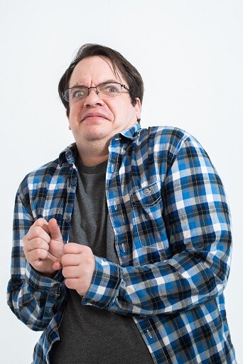 Image description: Kai, a white person in a plaid shirt and glasses, leans away and looks disgustedly into the camera.