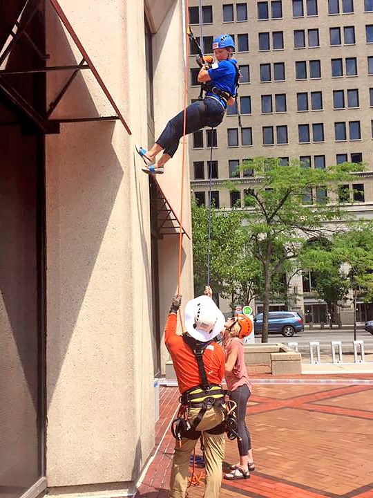 Woman almost done repelling down a building with two volunteers on the ground