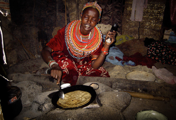 Rendille woman cooking over open fire with torch.