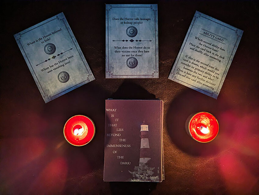 The deck of cards lies down, with three revealed cards by its side. The cards are surrounded by two lit candles in the dark