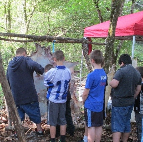 Students scrape a deerskin with stone tools at the hide tanning demonstration. This kind of hands-on learning is a focus for many of the LAW technology demonstrations.