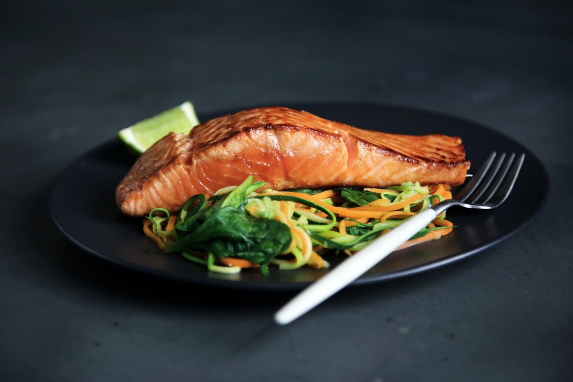 Salmon and greens on a plate with a fork and dark colored background